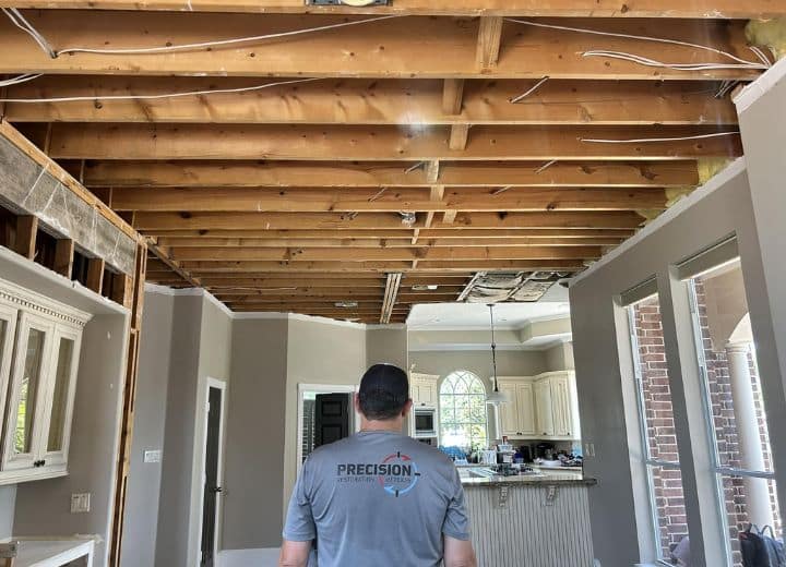 A technician from Precision Restoration inspects a home with its ceiling removed due to storm damage in Houston, Texas. The exposed beams and debris highlight the extent of interior storm damage repair work needed.