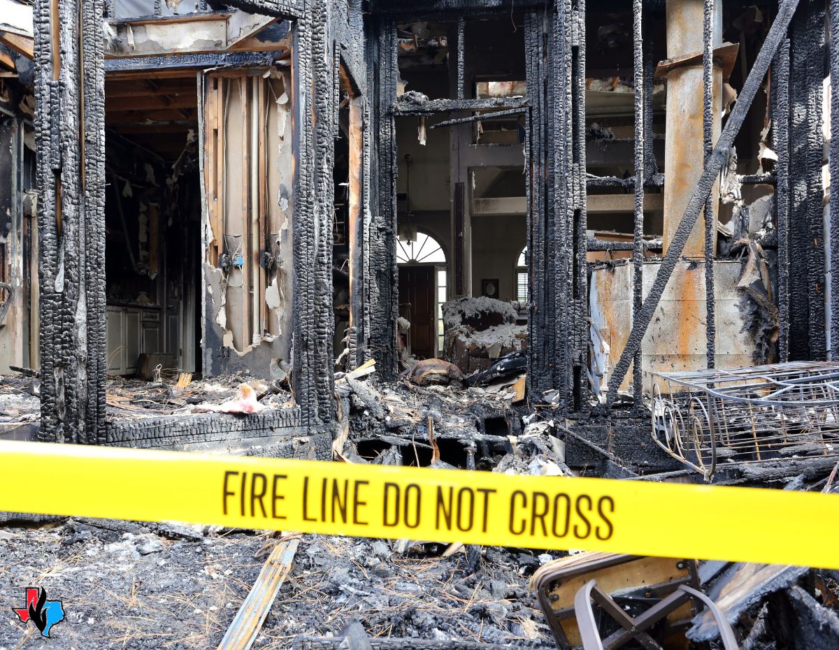 A fire-damaged house with charred walls and debris, surrounded by yellow "Fire Line Do Not Cross" tape. This image emphasizes the importance of securing the property and knowing what to do after a kitchen fire to prevent further damage and unauthorized access.