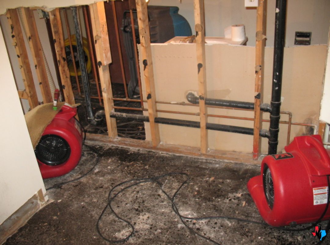 A water-damaged wall with exposed studs and drying fans during emergency water damage restoration in The Woodlands, TX. Restoration equipment is in place to prevent further moisture damage and mold growth.