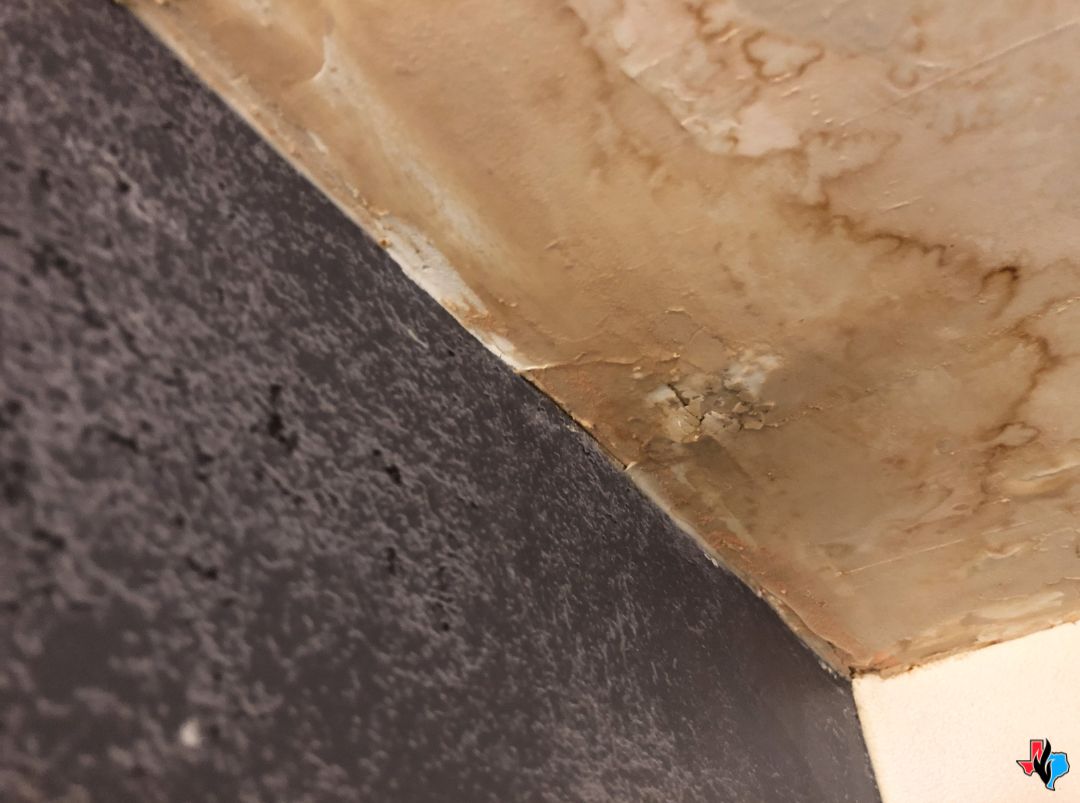 Water Damage Restoration in Pasadena, TX – Brown water stains and ceiling damage from a leak above a dark-colored wall. Precision Restoration provides 24/7 emergency water removal and repair services in Pasadena, TX.