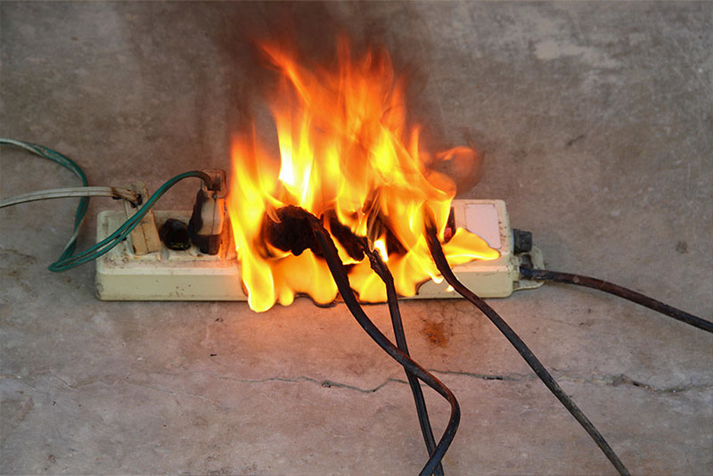 Power strip on fire with multiple plugged-in cords burning on a concrete floor.