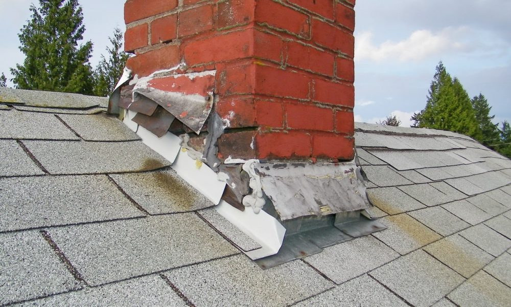 Damaged roof flashing around a brick chimney, showing signs of wear and water intrusion risk.