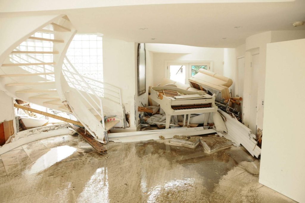 Severely water-damaged interior with collapsed staircase, broken furniture, and standing water on the floor.