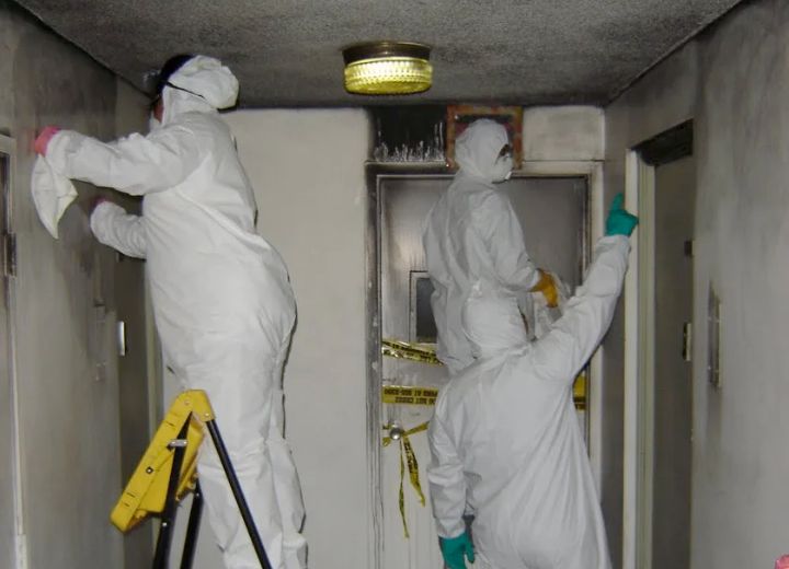 Crew in protective suits cleaning soot from walls after fire damage.