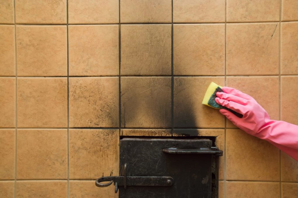 Hand in a pink glove scrubbing soot from a tiled wall with a sponge after fire damage.